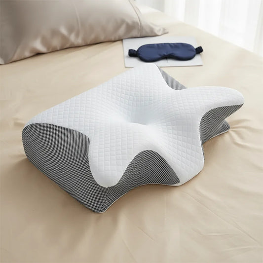 Oreiller cervical ergonomique IceRelief en mousse à mémoire de forme, forme papillon, posé sur lit beige avec masque de sommeil