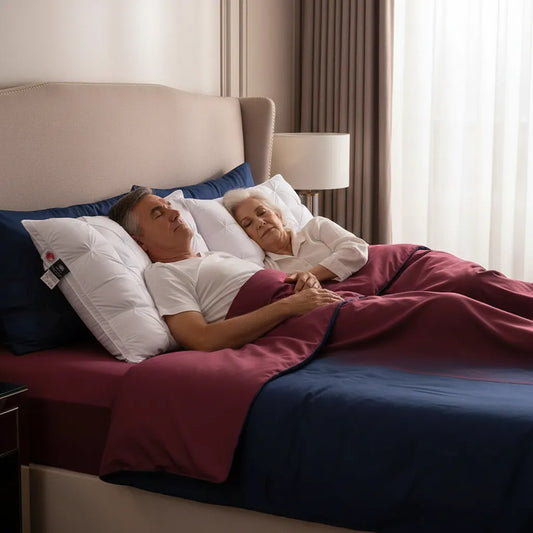 Couple de seniors dormant sur oreillers duvet d'oie luxe IceRelief losanges gonflés, lit king-size draps bleu marine ambiance hôtel 5 étoiles